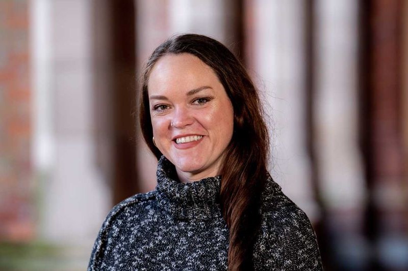 smiling woman with long dark hair wearing a chunky, black and white polo neck jumper in an outdoor setting